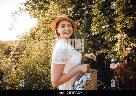 Bella donna in cappello che tiene il cesto con fiori Foto Stock