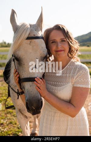 Ritratto di una giovane donna in abito bianco che abbraccia il cavallo Foto Stock