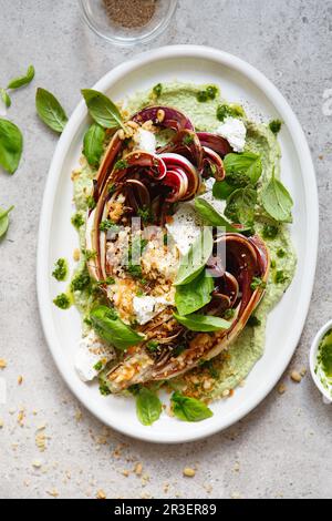 Insalata di radicchio arrosto con feta, tahini verdi, pinoli e pesto al basilico. Radicchio rosso di treviso tardivo, rosso chic italiano Foto Stock