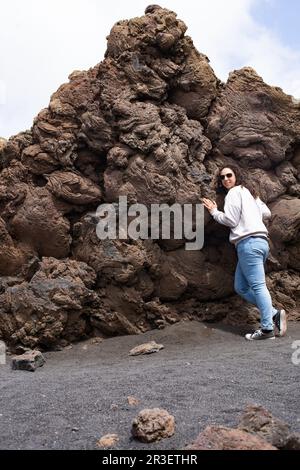 Giovane donna brunetta che sorride all'interno del Volcán del Cuervo di Lanzarote, Spagna, indossando jeans blu, sneaker nere e sneaker nere Foto Stock