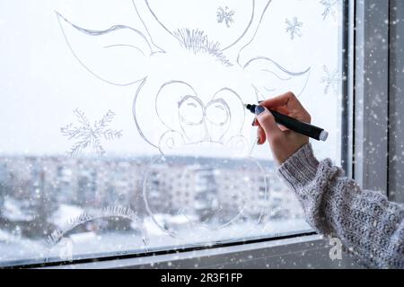 Pittura a mano femminile capriolo di Natale dipinto su vetro della finestra. Decorazioni invernali natalizie sul vetro della finestra. Disegno bianco di cervo. Foto Stock