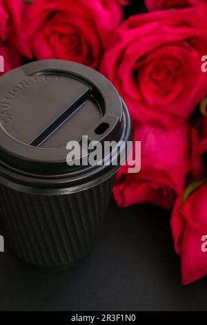 Eco tazza di carta nera con rose rosa sullo sfondo. Concetto di vacanza. Bere caffè della mattina da una tazza riutilizzabile. Zero sprechi take a Foto Stock