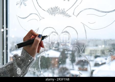 Pittura a mano femminile capriolo di Natale dipinto su vetro della finestra. Decorazioni invernali natalizie sul vetro della finestra. Disegno bianco di cervo. Foto Stock