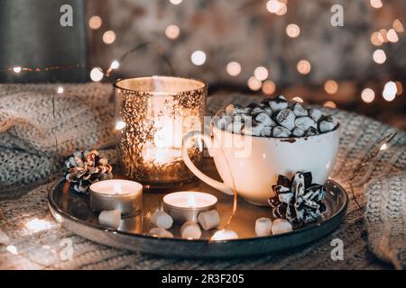 Tazza con cacao caldo invernale e marshmallows a letto. Luci di Natale. Decorazione coni di pino. Foto Stock