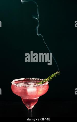 Cocktail di tipo margarita alcolico o non alcolico con ghiaccio e rametto di rosmarino fumante su sfondo scuro Foto Stock