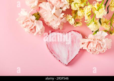 Bouquet di garofani rosa e mattiola gialla con cuore decorativo. Design concetto di saluto vacanza con bouquet garofano Foto Stock