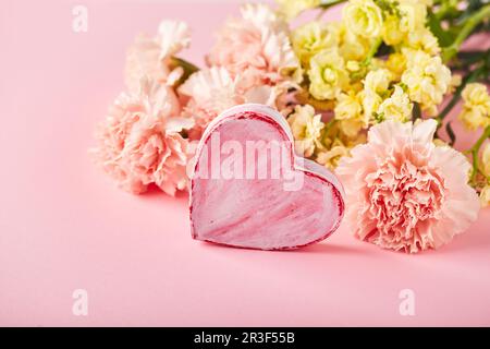 Bouquet di garofani rosa e mattiola gialla con cuore decorativo. Design concetto di saluto vacanza con bouquet garofano Foto Stock