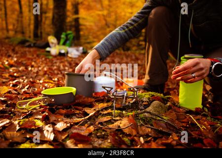 La donna usa un riscaldatore a gas portatile e una padella per cucinare all'aperto Foto Stock