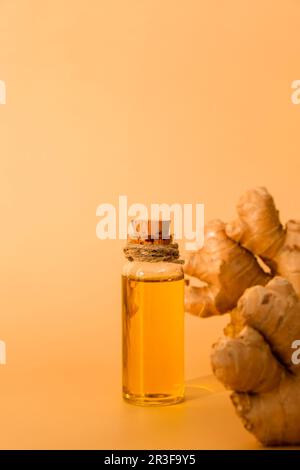 Bottiglia di vetro di olio essenziale di zenzero, radice di zenzero su fondo beige. Concetto di alimentazione sana. Zingiber officinale Essentia Foto Stock