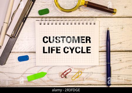 Sul blocco note per scrivere il testo Customer Life Cycle, lente di ingrandimento, grafici e occhiali Foto Stock