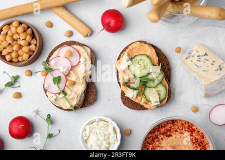 Deliziosi sandwich con hummus e diversi ingredienti su sfondo bianco, piatto Foto Stock