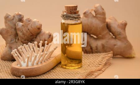 Bottiglia di vetro di olio essenziale di zenzero, radice di zenzero su fondo beige. Vita alternativa sana. Ingredienti cosmetici naturali Foto Stock