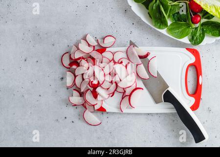 Le fette si irradiano su un tagliere di plastica bianca, spinaci per bambini e lattuga su uno sfondo di pietra grigio chiaro, vista ravvicinata Foto Stock