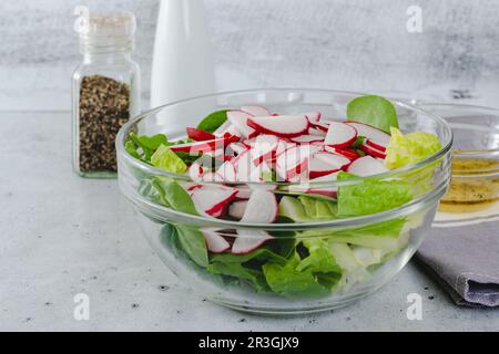 Insalata di primavera in un recipiente di vetro primo piano sul tavolo da cucina. Impasto di ravanello fresco, lattuga romana e spinaci per bambini Foto Stock