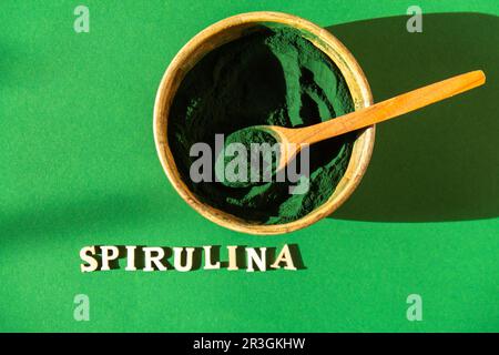 Polvere di spirulina di alghe blu-verdi in ciotola ecologica di bambù con testo SPIRULINA. Polvere super in cucchiaio. Fonte di integratore alimentare di prote Foto Stock