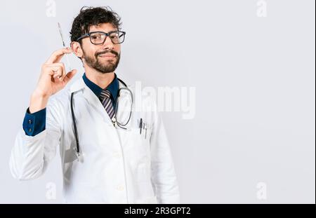 Giovane medico che tiene una siringa isolata. Medico sorridente che tiene una siringa su sfondo isolato. Concetto di medico e vaccino Foto Stock