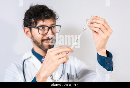 Bel medico che attinge la medicina da una fiala isolata. Giovane medico che aspira la medicina da un flaconcino isolato. Concetto di medico con antidoto malattia Foto Stock