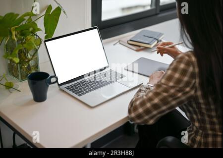 Primo piano immagine posteriore di una donna asiatica che gestisce il suo lavoro alla sua scrivania nel suo spazio di lavoro minimo. computer portatile schermo bianco mockup Foto Stock