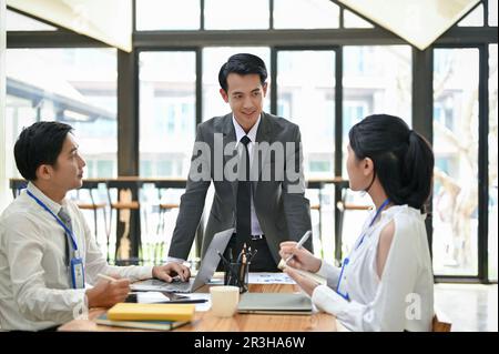 Un capo maschio asiatico professionale e di successo conduce l'incontro con il suo team nella sala riunioni. Concetto di business Foto Stock