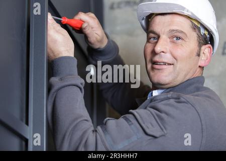 un lavoratore maschio felice usa un cacciavite per stringere il finestrino Foto Stock