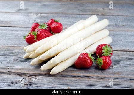 Fragole rosse mature e asparagi bianchi provenienti da agricoltura biologica offerti in primo piano su una vecchia tavola rustica di legno Foto Stock