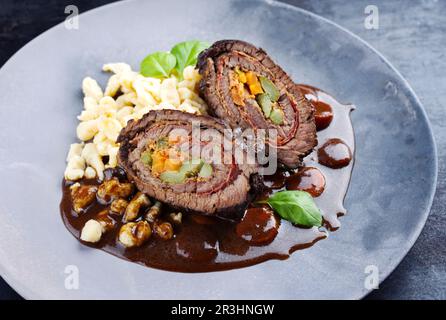 Tradizionali involtini di manzo di wagyu tedesco cotti a cottura lenta con spaetzle serviti in salsa piccante come primo piano su un piatto di design Foto Stock