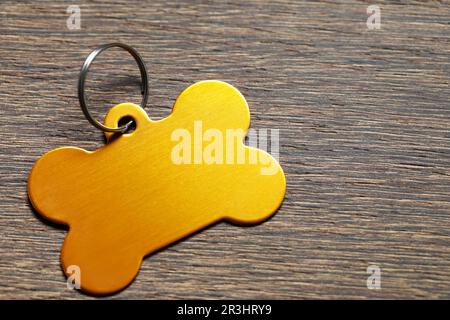 Cartellino in metallo giallo a forma di osso su tavolo in legno, primo piano. Spazio per il testo Foto Stock