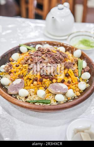 Un piatto uzbeko chiamato pilaf. Riso con carne, carote, cipolle, uova e kazy in un piatto di astau sulla tavola. Un piatto tradizionale uzbeko chiamato pilaf. A. Foto Stock