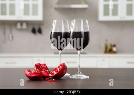 Bicchieri di vino rosso e melograno fresco sul banco in cucina Foto Stock