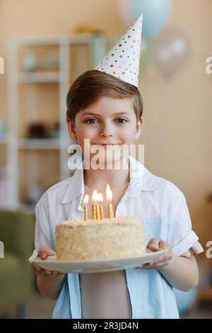 Verticale vita in su ritratto di ragazzo felice tenendo torta di compleanno con candele e guardando la fotocamera Foto Stock