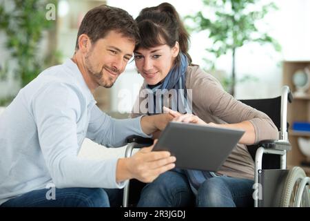 un uomo attento e una donna disabile che utilizzano un tablet digitale Foto Stock