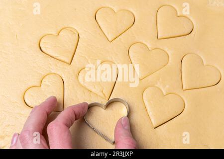 Taglierine per biscotti a forma di cuore che tagliano le vacanze. Come tagliare i biscotti a forma di cuore dall'impasto. Cucinare una deliziosa e salutare colazione di vacanza naturale Foto Stock