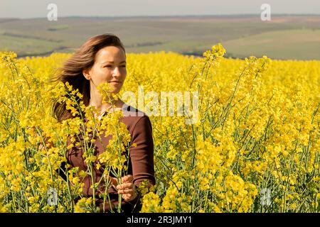 Una giovane donna caucasica entrò in un campo di fiori gialli alti e fiorenti, un campo di colza che evocava emozioni di gioia, ammirazione e pacificazione Foto Stock