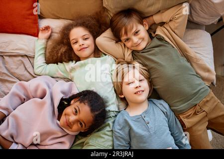 Vista dall'alto di un gruppo di bambini sdraiati sul letto insieme e guardando la macchina fotografica Foto Stock