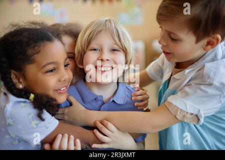 Gruppo di bambini diversi abbracciano felicemente mentre giocano insieme e sorridono Foto Stock