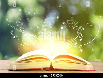 Musica che scorre dal libro. Simboli musicali che volano su tome su un tavolo di legno contro sfondo sfocato Foto Stock