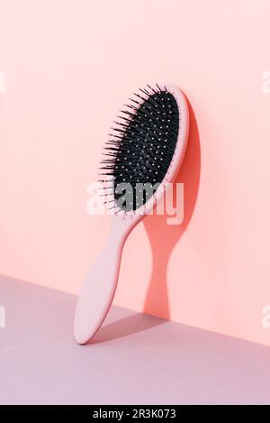 Spazzola per capelli a pale su sfondo rosa e grigio con ombra dura, primo piano Foto Stock