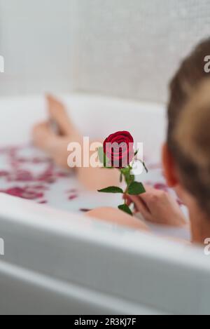 La donna si rilassa in un bagno con latte e petali di rosa. Foto Stock