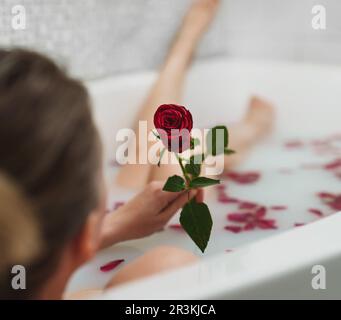 La donna si rilassa in un bagno con latte e petali di rosa. Foto Stock