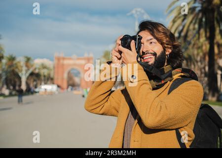 Felice fotografo turistico sorridente e scattando una foto in via Barcellona. Giovane viaggiatore che si concentra con la fotocamera un monumento in Europa in un viaggio. Uomo bearded godendo il suo tempo libero di fine settimana. Foto di alta qualità Foto Stock