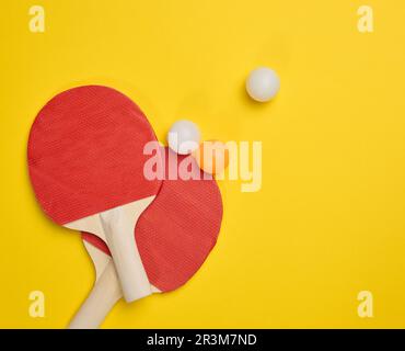 Coppia di racchette da tennis in legno per ping pong e palle di plastica su sfondo giallo Foto Stock