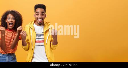 Due amici acclamano e sostengono il compagno sulla concorrenza urlando gioiosamente pugni clenching in sostegno fugure sorridendo ampiamente wa Foto Stock