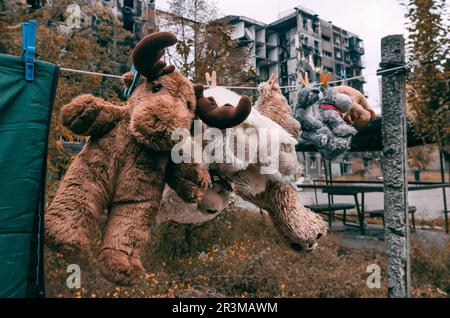 I giocattoli morbidi vengono asciugati dopo il lavaggio sullo sfondo di un edificio bruciato a Mariupol Foto Stock