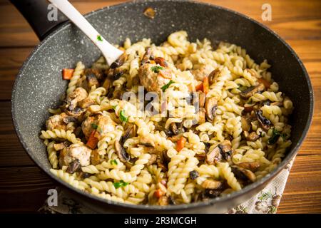 vermicelli cotti con funghi, carne e verdure in padella su un tavolo di legno Foto Stock