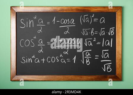 Lavagna con molte formule matematiche diverse sulla parete verde Foto Stock