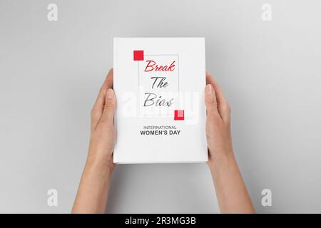 Libro di tenuta della donna con titolo Break the Bias dedicato alla Giornata internazionale della donna contro sfondo grigio chiaro, primo piano Foto Stock