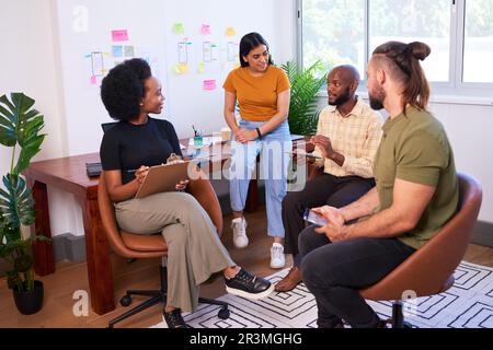 Quattro diversi membri del team che hanno una riunione informale, seduti in un ufficio creativo Foto Stock