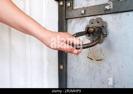 La mano di una donna apre una porta antica. Maniglia della porta a forma di anello Foto Stock