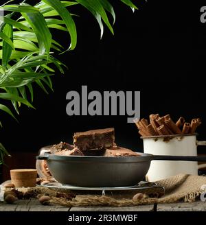 Pezzi di torta di brownie al cioccolato al forno con noci in una padella di metallo nero su un tavolo di legno Foto Stock