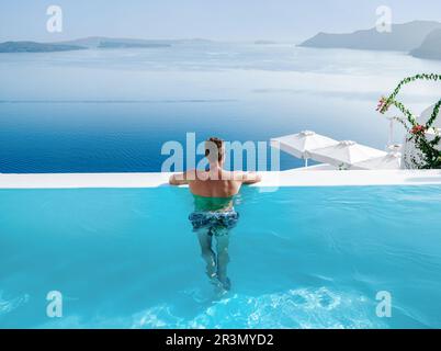 I giovani nuotano in breve relax nella piscina che si affaccia sulla caldera di Santorini Grecia Foto Stock